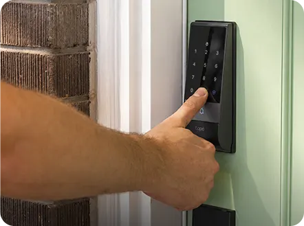 A finger placed on a smart lock fingerprint sensor next to a door frame